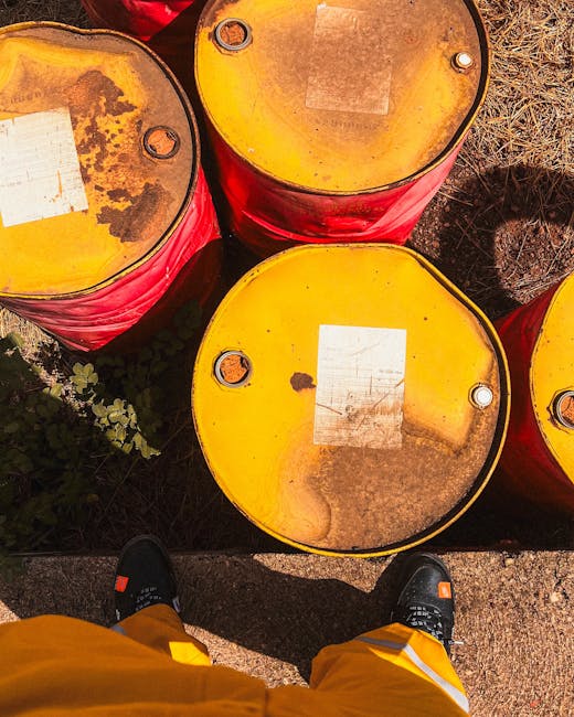 A large outdoor storage area filled with numerous plastic drums and barrels, primarily white with orange and black lids. The barrels are arranged in rows, with some standing upright and others lying o